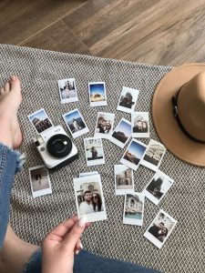 Molte foto Polaroid sparse sul pavimento con il piede di una ragazza vicino.